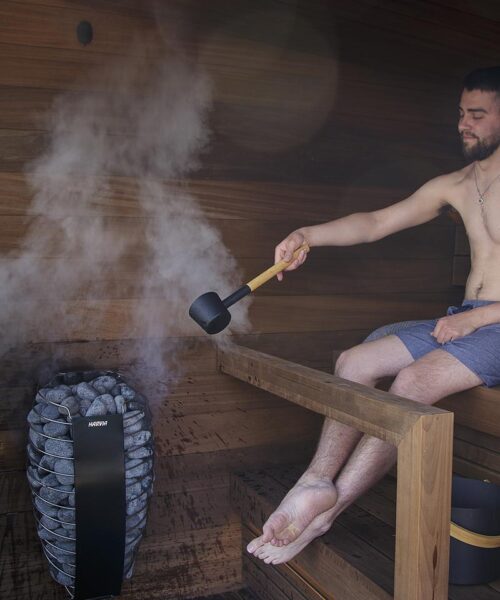 Man sits in sauna pouring water on the Harvia Spirit sauna heater